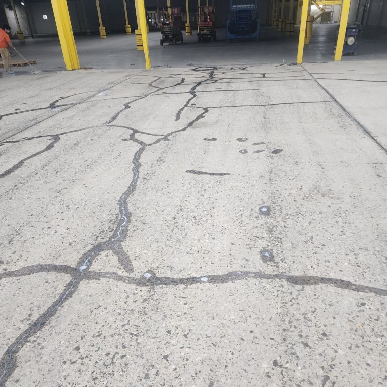 Severely cracked concrete warehouse floor requiring heavy-duty mechanical surface preparation before epoxy coating installation.