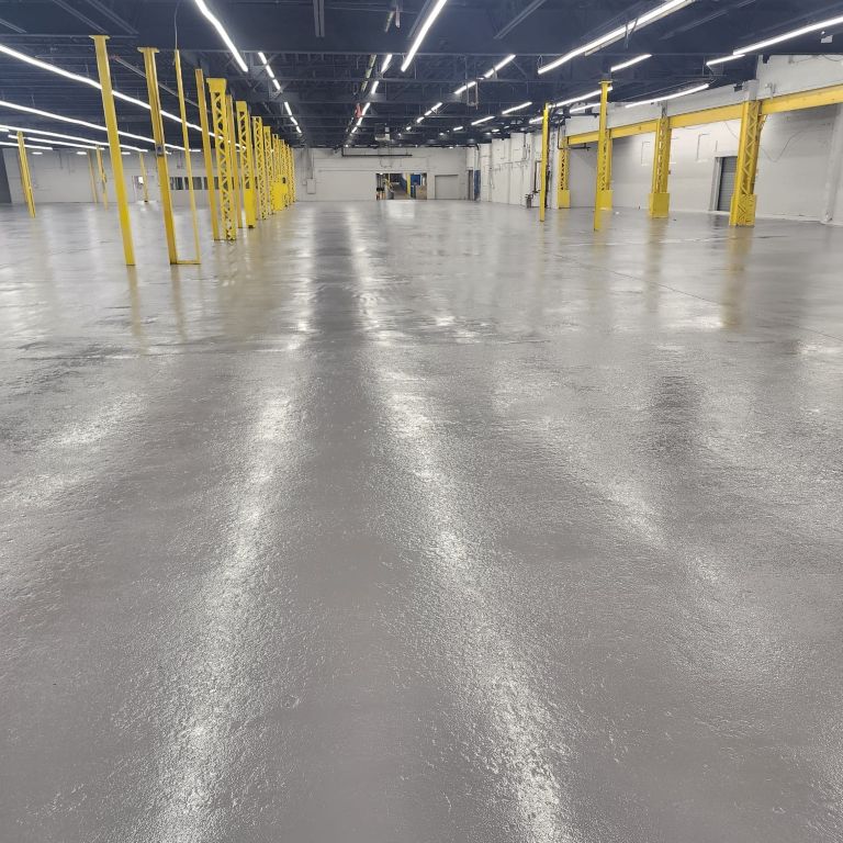 High-gloss industrial warehouse epoxy flooring installation in a Central Jersey facility featuring reflective seamless coatings and safety pillars.