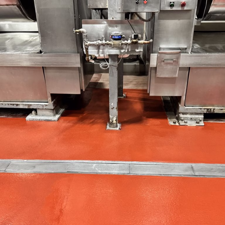 Close-up of stainless steel equipment posts anchored onto a seamless thermal shock resistant urethane concrete floor in a commercial kitchen.